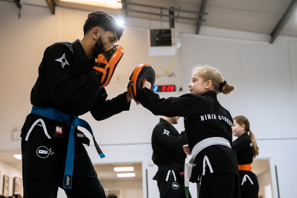 Female Ninja School student punches a pad held up by an instructor.