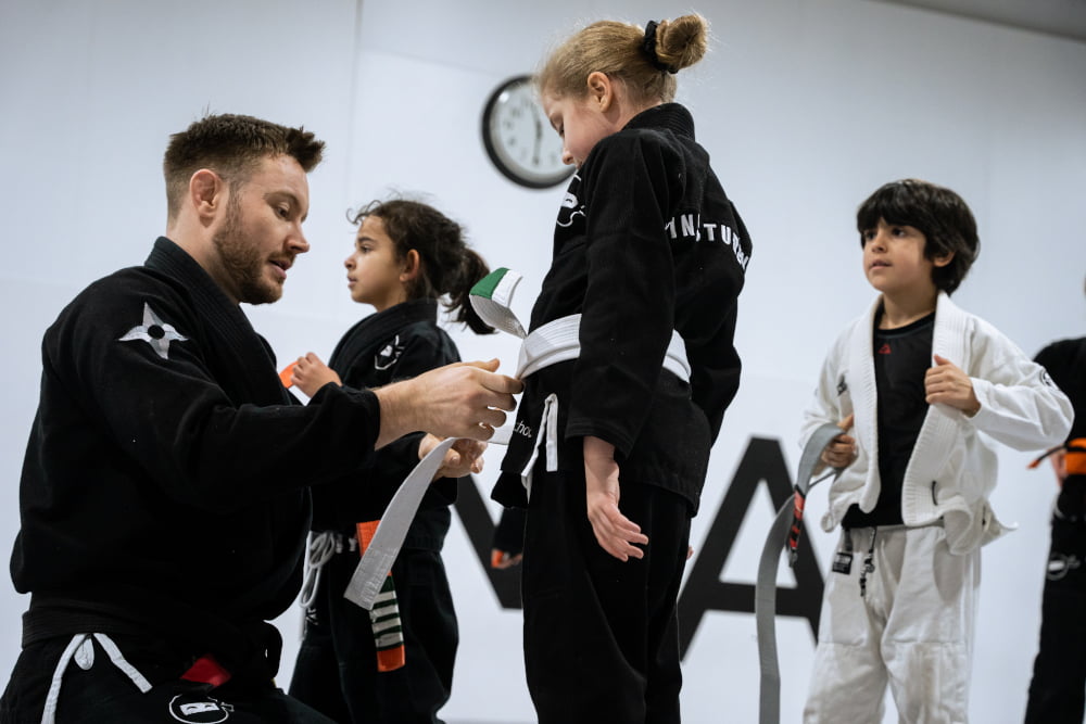 A ninja school instructor rewards a student with a new belt.