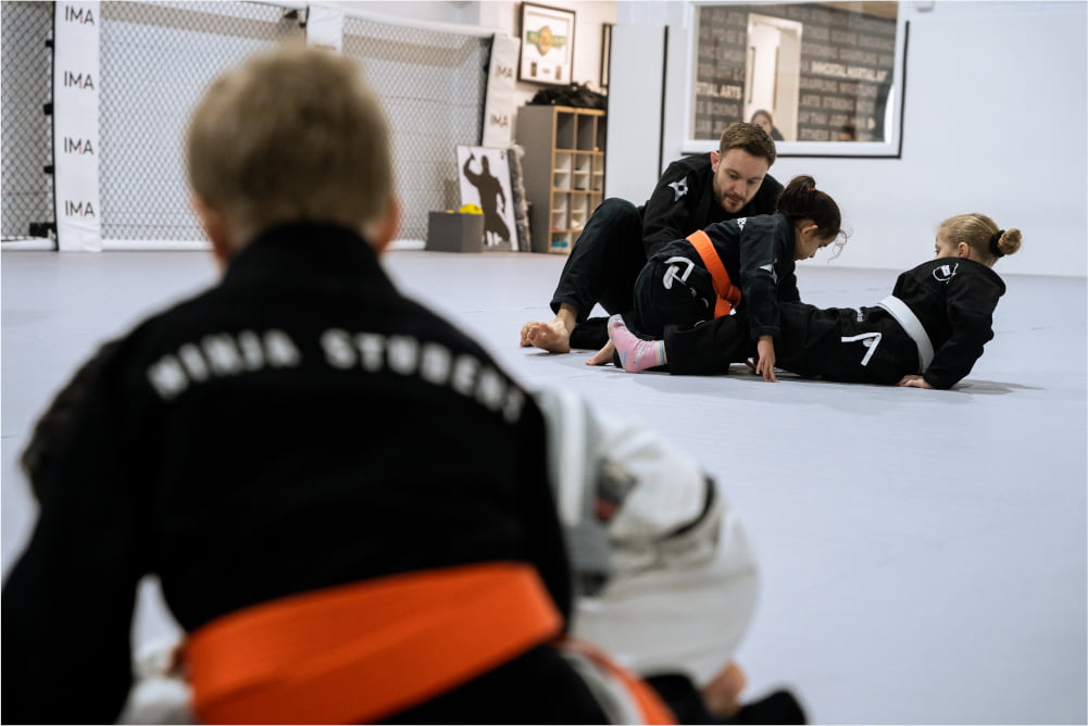 A ninja school student watches as an instructor helps two other students learn a jiu jitsu technique.